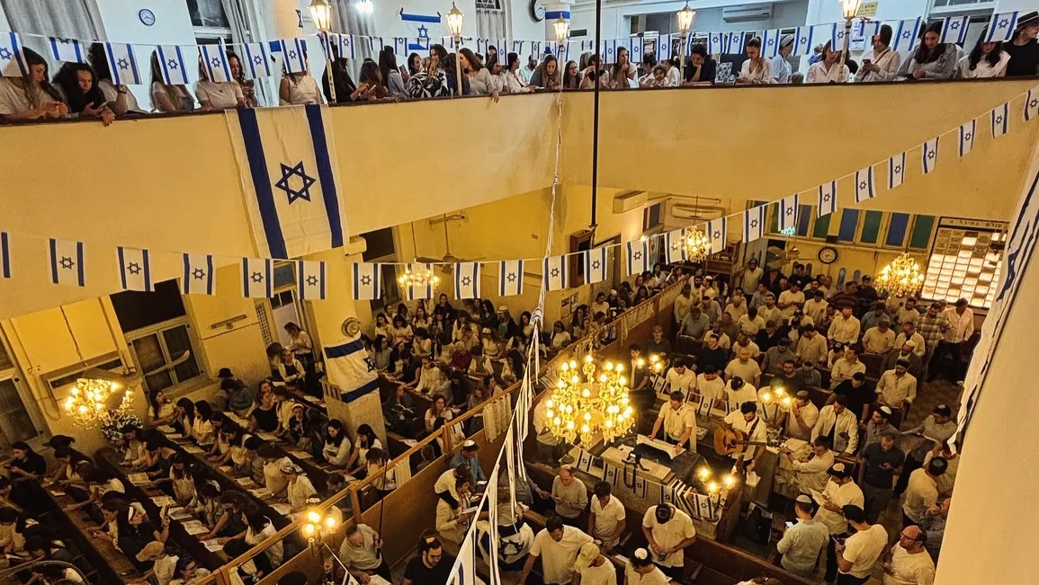 The packed main sanctuary of 126 Ben Yehuda synagogue in Tel Aviv, strung with Israeli flags for an Independence Day service, seen from the women's gallery.