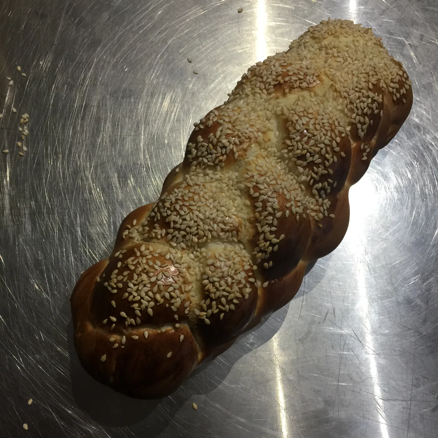 A golden-brown baked loaf dusted with sesame seeds cooling on a steel surface