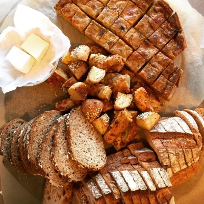 A spread of artisan breads, sourdough, focaccia and rolls, with butter on a wooden board