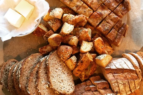 A spread of artisan breads, sourdough, focaccia and rolls, with butter on a wooden board
