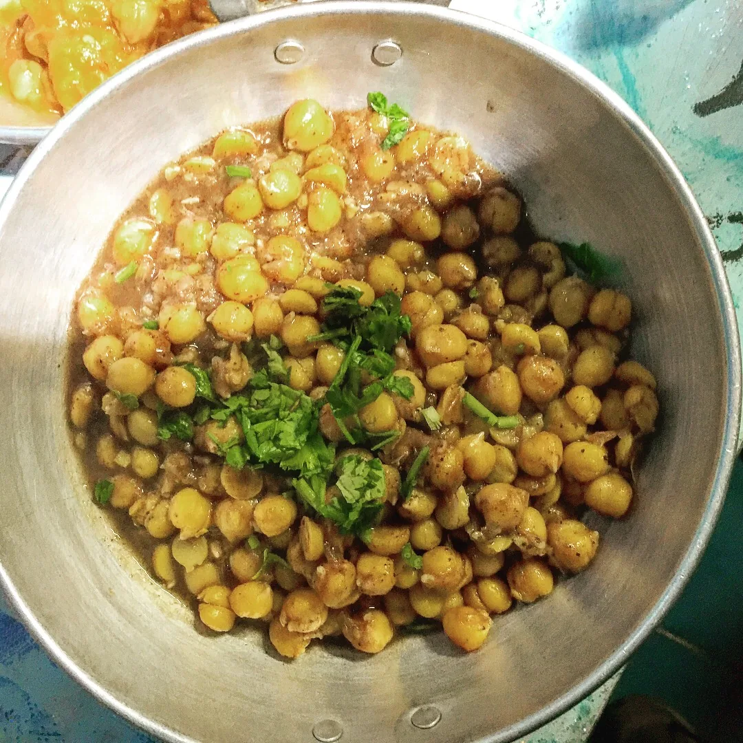 A metal bowl of warm chickpeas topped with fresh coriander at Hummus el Abed Abu Hamid in Old Akko