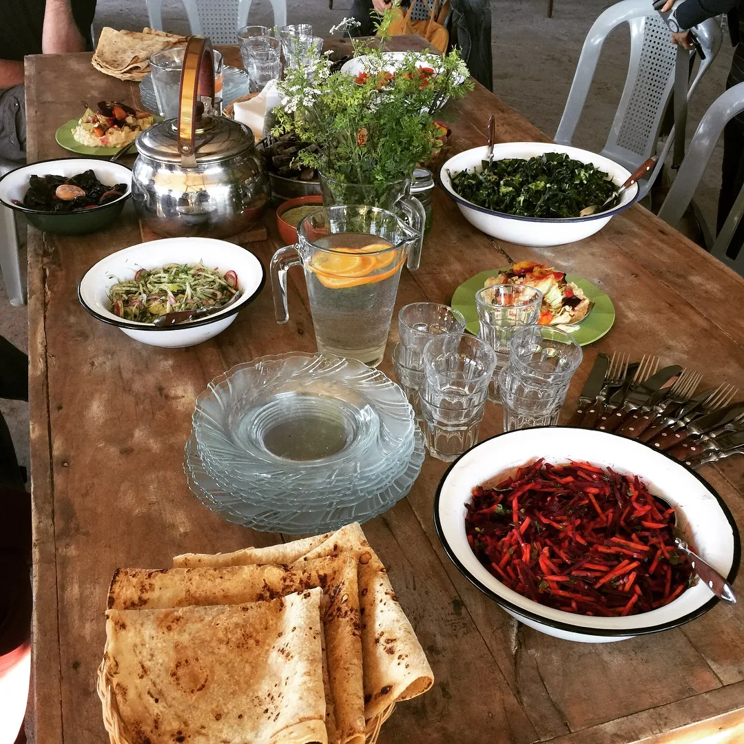 A worn wooden table laid with bowls of beetroot and carrot salad, cooked greens and flatbread, the meal at the Kaima farm in Beerotayim