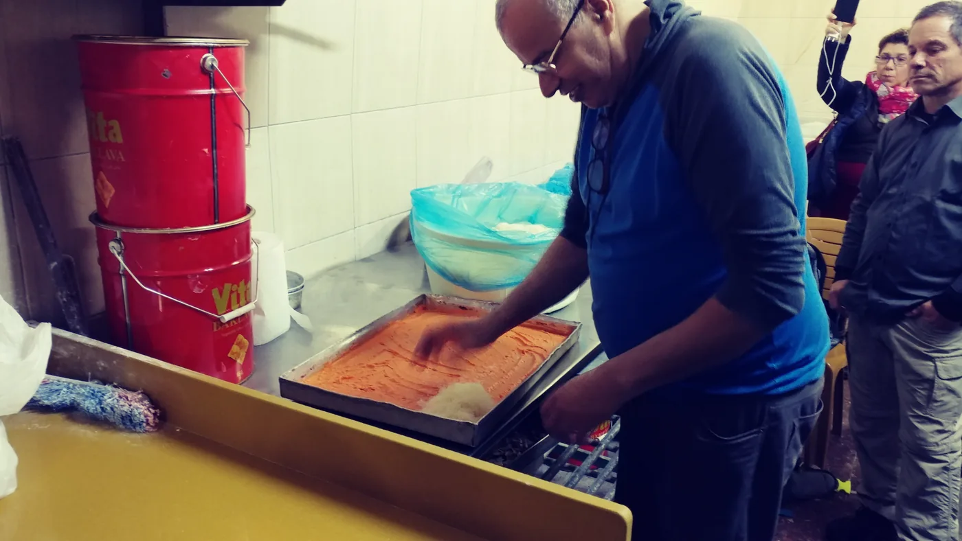 A pastry maker spreading knafeh filling and demonstrating to a visiting group