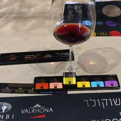 A glass of red wine beside squares of Valrhona dark chocolate on a marble tasting bar