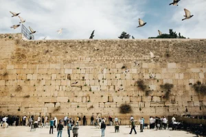 Doves in flight above the Western Wall in Jerusalem, with people praying at the stones along the foot of the wall.