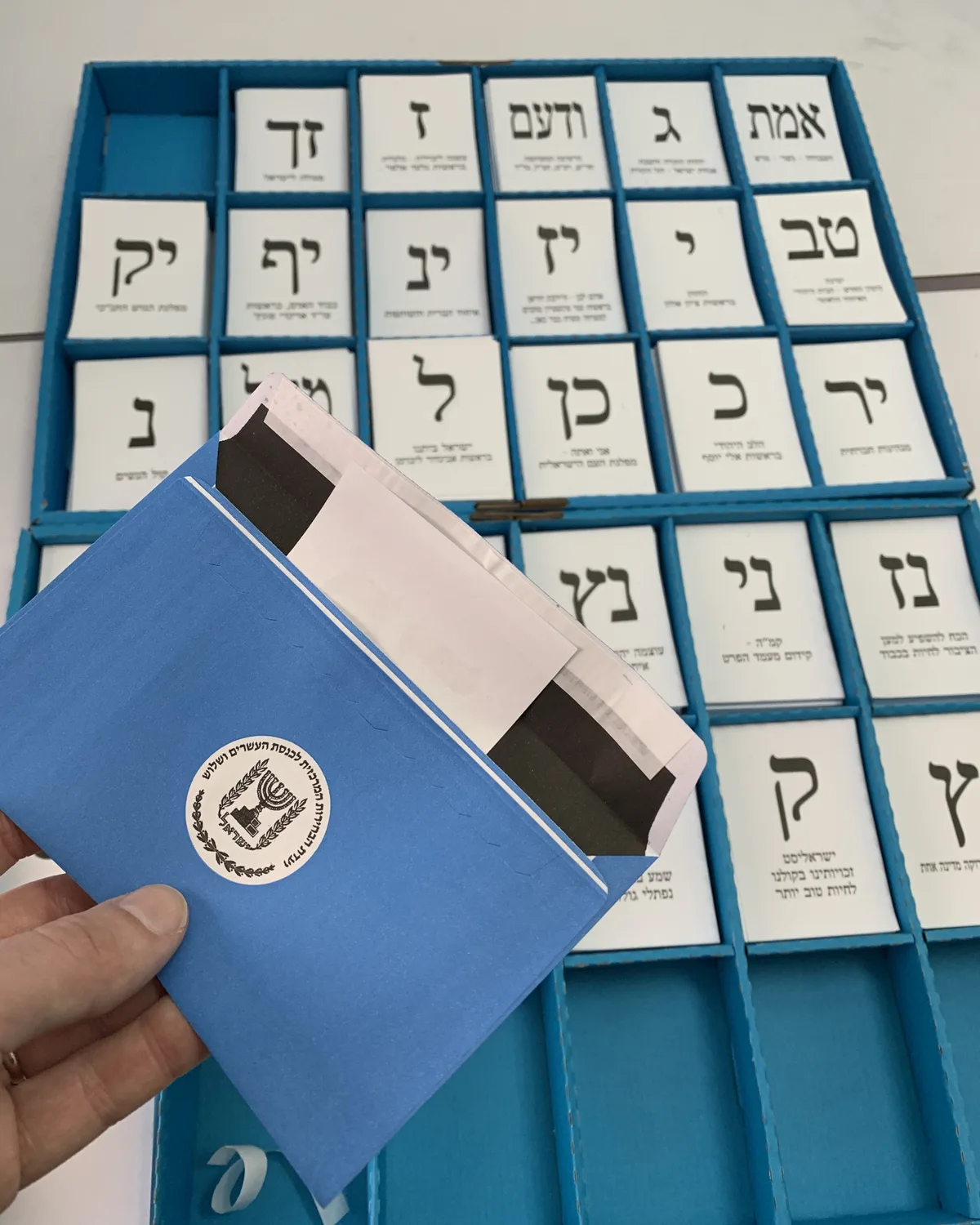 A ballot slip going into the blue official envelope in front of the tray of party slips, 2020.